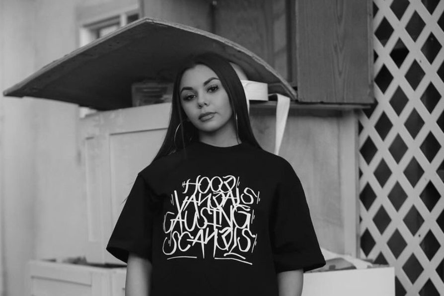Person wearing a black t-shirt with text, standing outdoors.